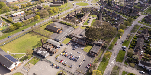 This image: An aerial view of the site taken from the north, showing the car park in the foreground.
						 The map: bird's eye view of the site, bounded by a red line, along Knowles Road, Charnor Road,
						 and the school to the north. The A563 roundabout can be seen to the south.